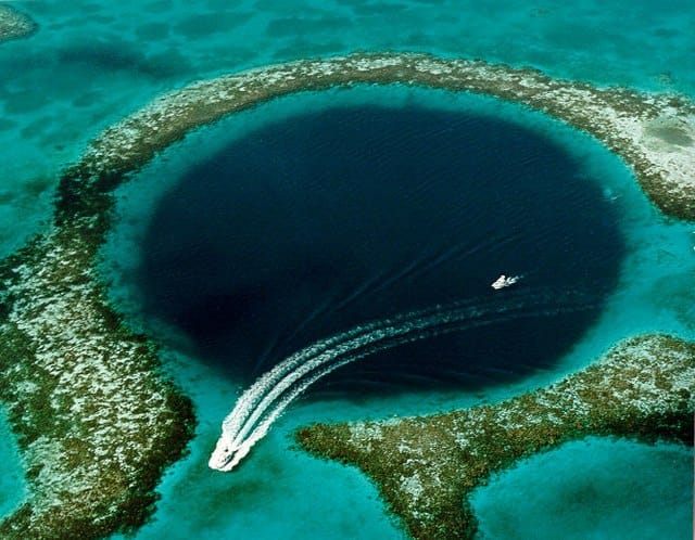 An aerial photo of the Great Blue Hole in Belize with a boat passing on top